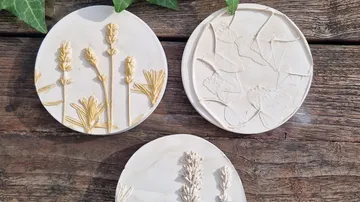Drei botanische Untersetzer aus Lehm auf Holz.